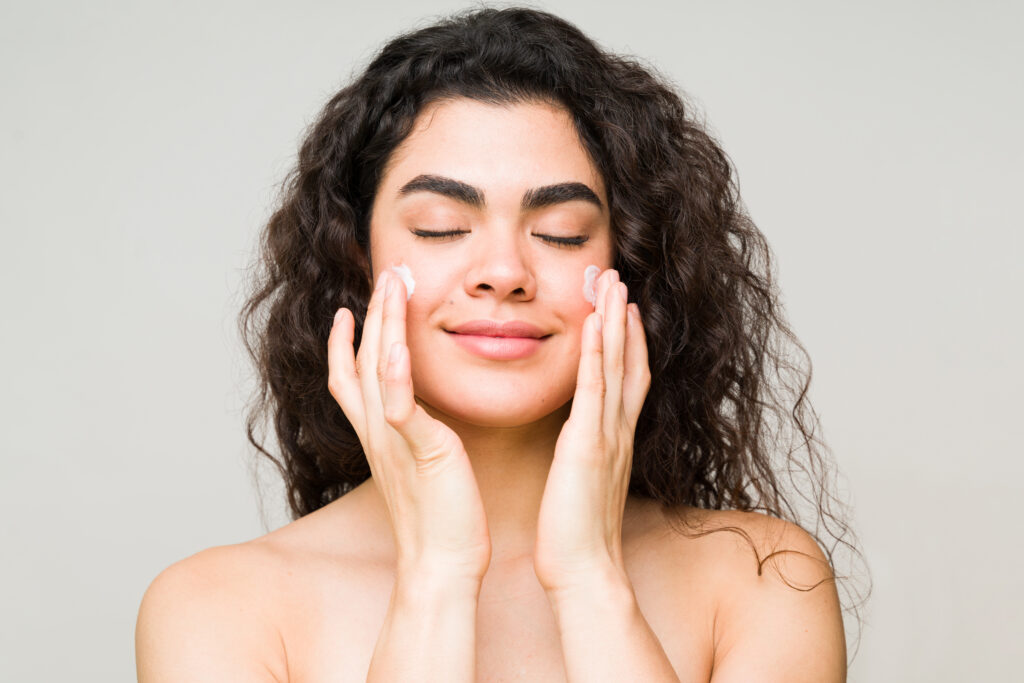 Beautiful young latin woman feeling relaxed after showering. Woman in her 20s putting moisturizing face cream for her perfect skin