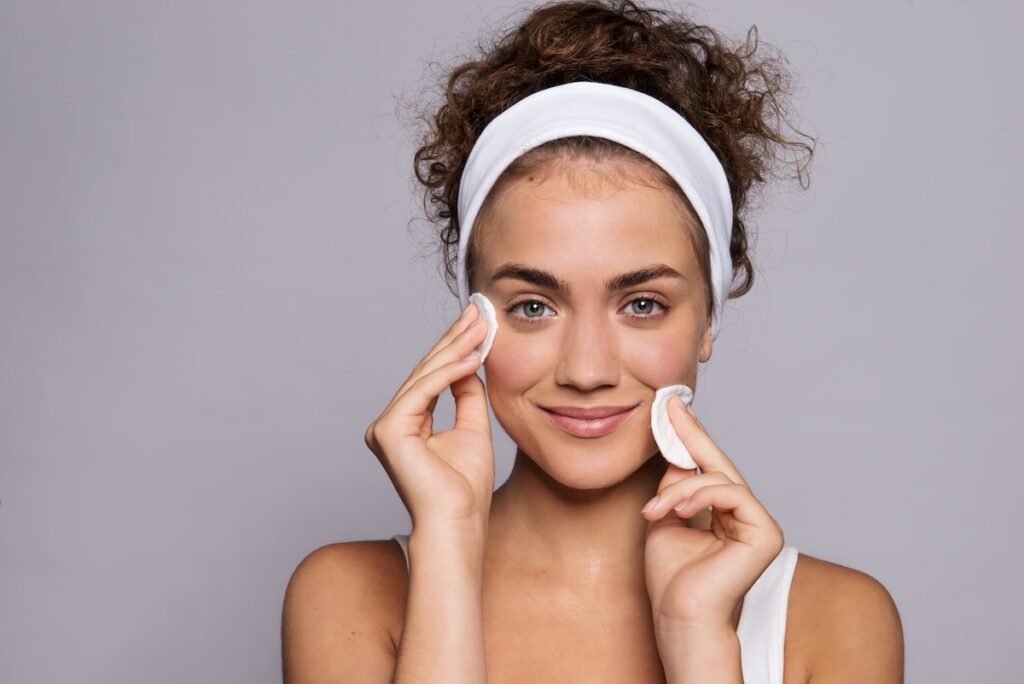 Smiling woman cleansing her face with cotton pads, preparing her skin for a Botox or dermal filler appointment to achieve smooth, natural results.