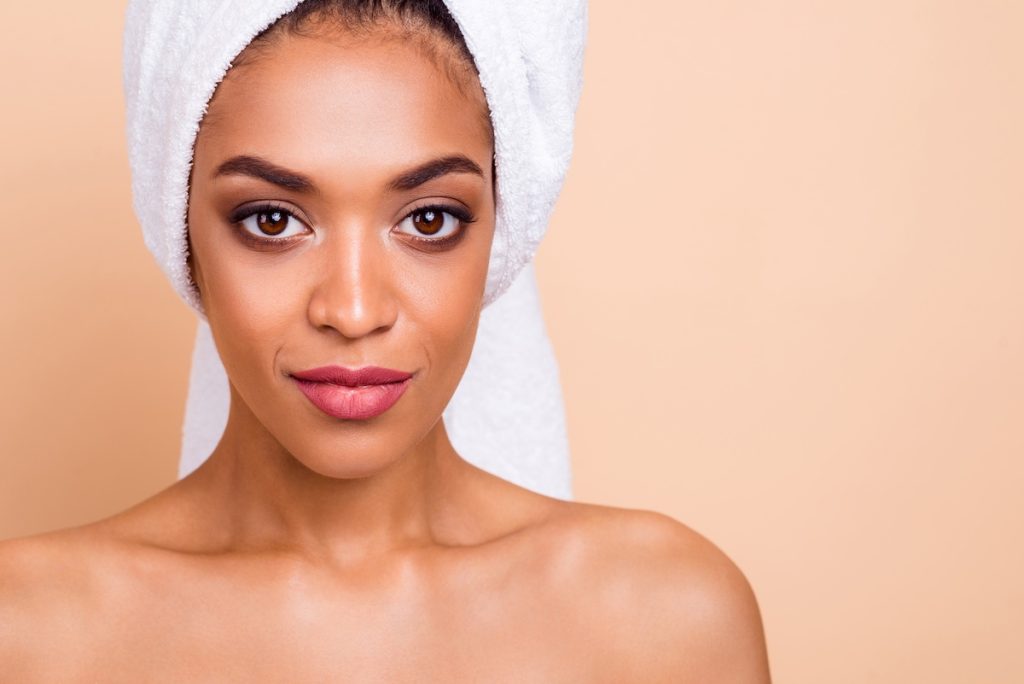 Cropped close-up portrait of her she nice-looking attractive perfect shine well-groomed lady clean clear flawless smooth silky soft skin laser peeling isolated on beige pastel background Woman with glowing skin and towel-wrapped hair against a soft peach color background.