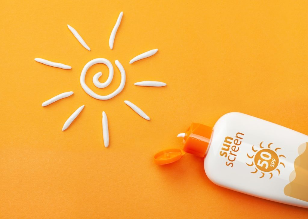 Sunscreen on orange background. Plastic bottle of sun protection and white sun-shaped cream.