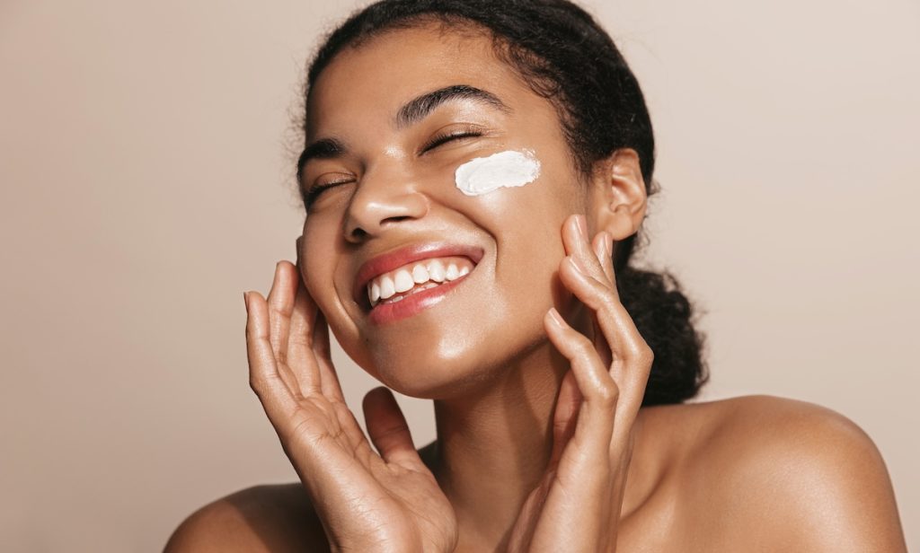 Smiling woman using skincare products to prepare her skin for summer.