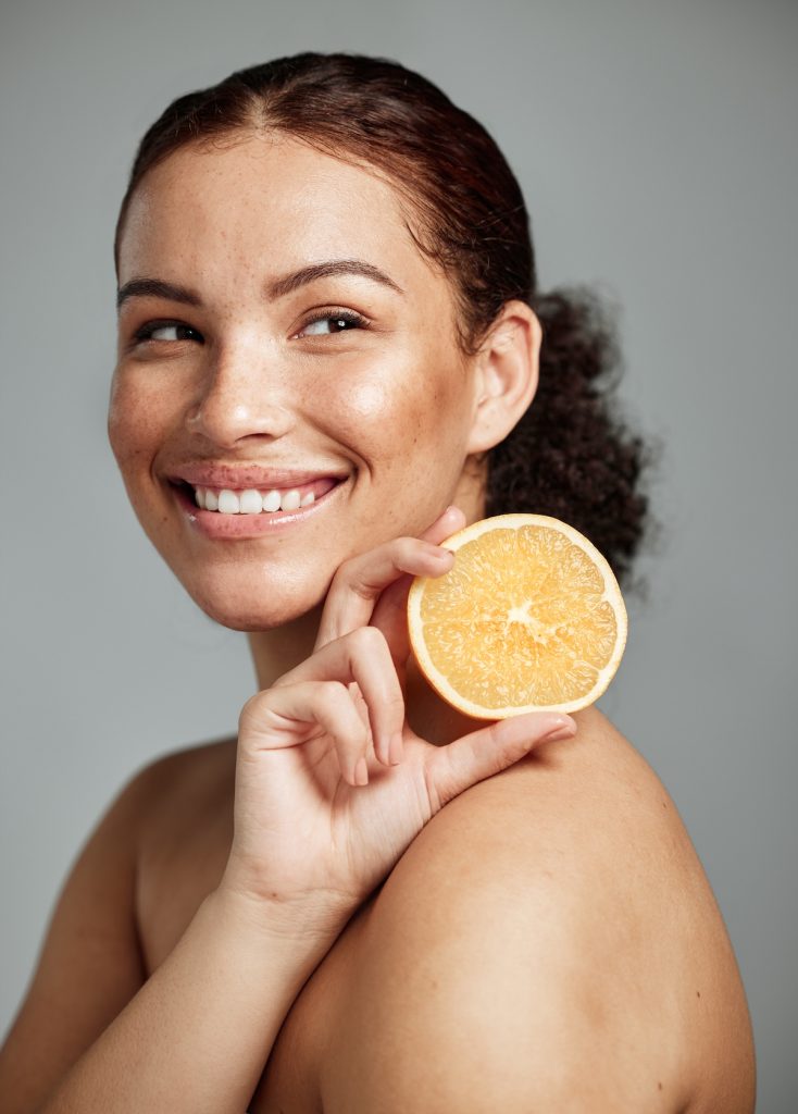 miling woman with glowing skin holding half an orange, symbolizing how healthy foods rich in vitamin C can promote radiant, healthy skin.