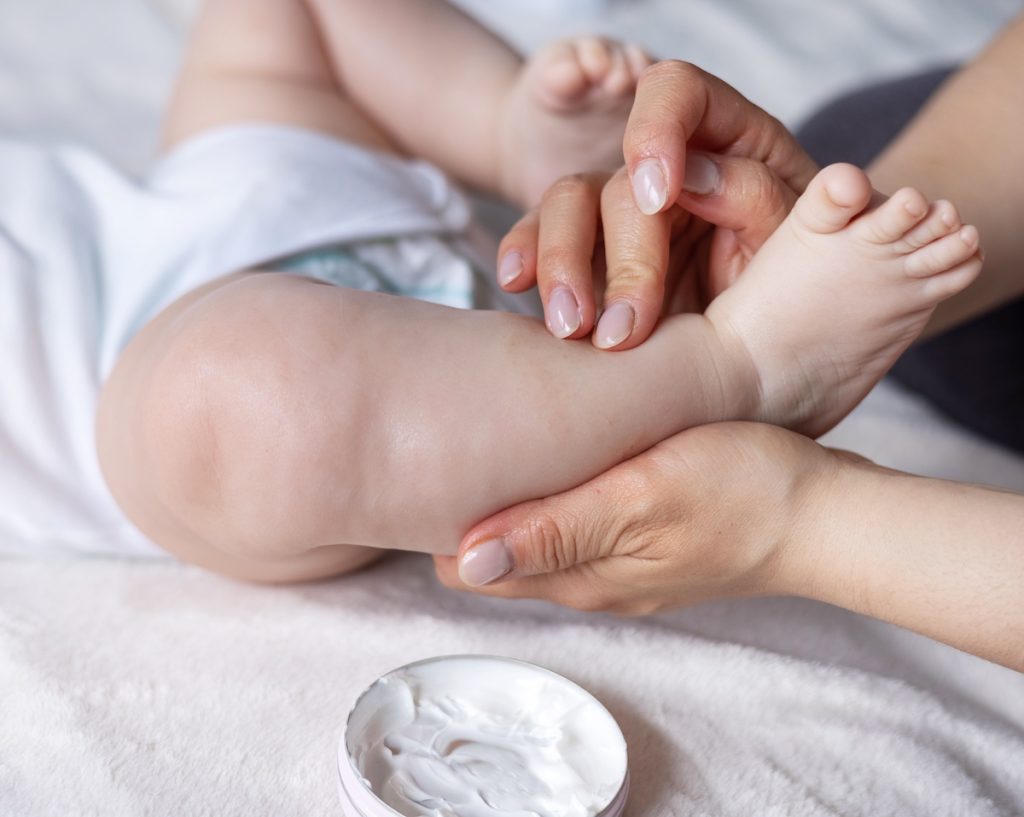Parent applying moisturizing cream to baby's leg and foot for winter dry skin relief