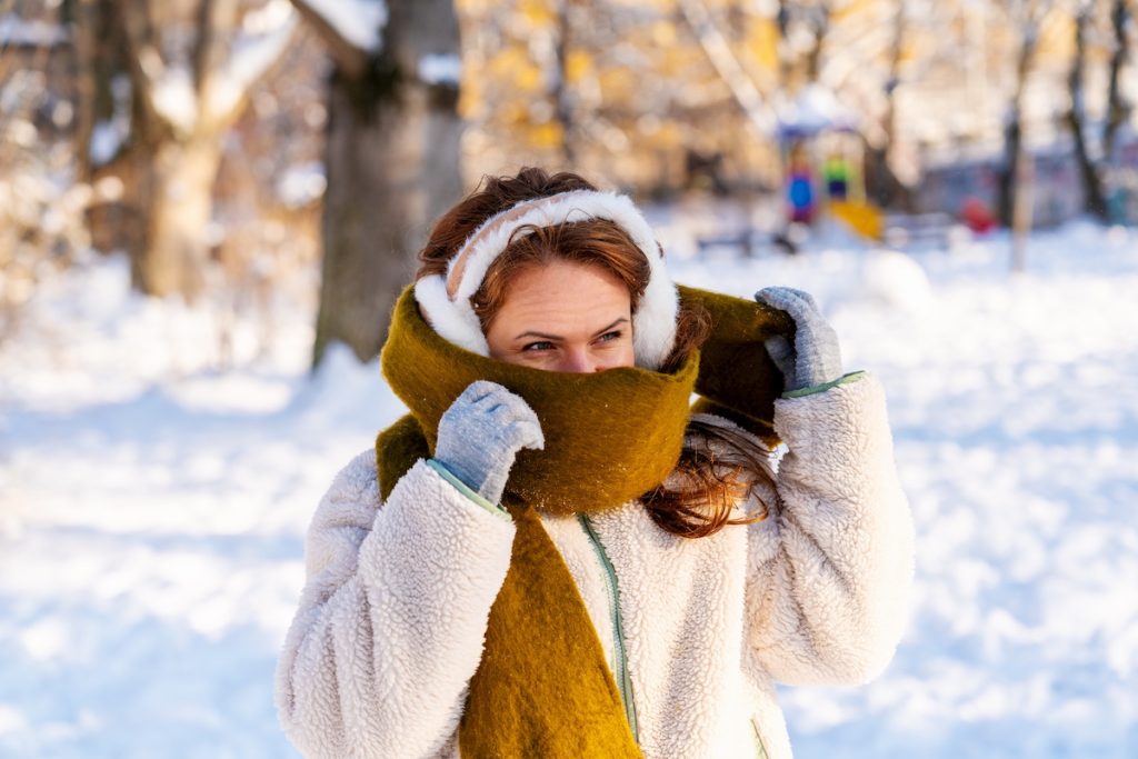 Portrait of woman wrapping herself in warm scarf during cold winter day